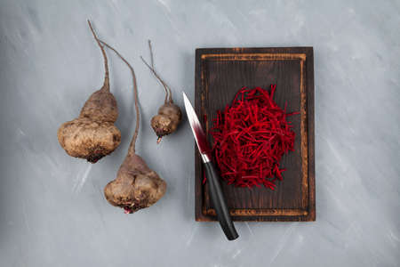 Ugly vegetables of abnormal shape. Crooked funny beetroot on a brown chopping Board. Gray background, selective focus, copy space. Concept - Food waste reduction. Using in cooking imperfect products.の写真素材