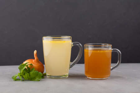 Two types of bone broth in transparent cups on a dark background. Fish and meat broth contain healthy collagen.の写真素材