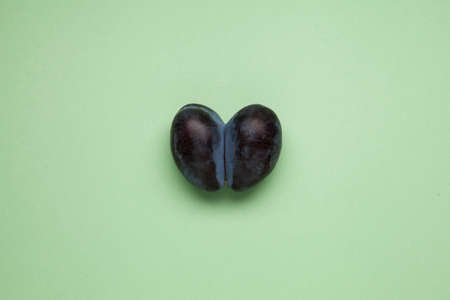 Double conjoined plum in form heart on a green background. Ugly prune. Flat lay, top view, copy space. Concept - Food waste reduction. Using in cooking imperfect products.の写真素材