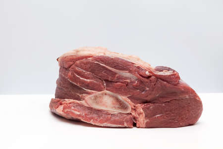Fresh large piece of meat. Juicy beef with a bone for broth on white table. Close-up, space for...