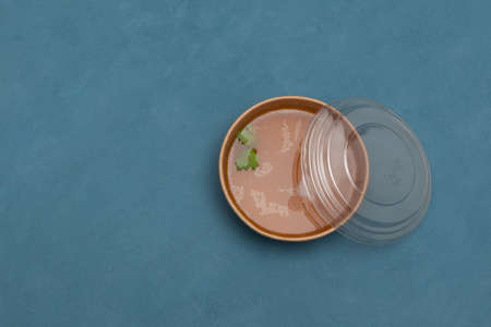Bone broth with natural collagen in a disposable paper bowl. Food delivery or takeaway. Blue background, copy space.の写真素材