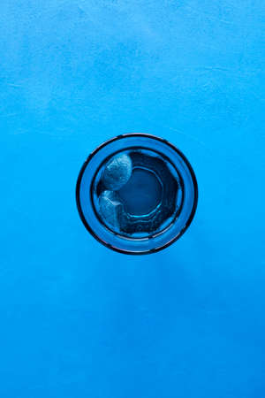 Drinking water with ice in transparent blue glass on blue background. Top view, selective focus, copy space.の写真素材