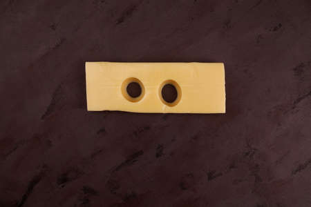 Piece of cheese with two big, funny holes like eyes. Top view, copy space.