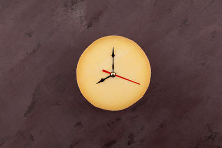 Clock hands on cheese head. Top view, brown background, copy space. Concept - interval fasting or...