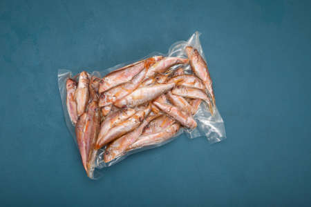 Frozen fish Red mullet (Goatfish) in plastic bag on blue background with copy space. Top view....