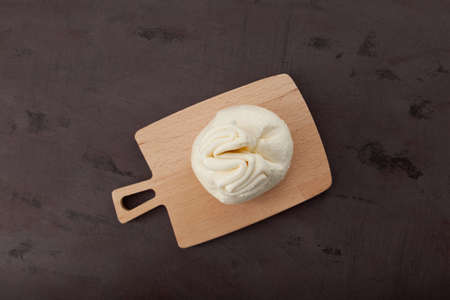 Italian soft cheese on cutting board, top view. White ball of burrata or burratina cheese made from mozzarella and cream filling. Brown background, copy space.の写真素材