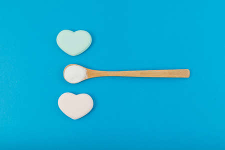 White powder in wooden spoon on blue background with hearts. Top view, copy space.