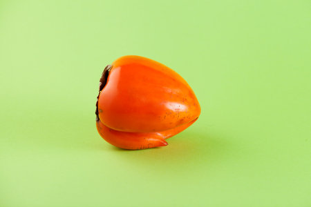 Ugly persimmon on green background with copy space. Intergrown double fruit. Funny, unnormal vegetable or food waste concept.の写真素材