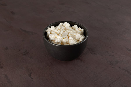Fresh natural Cottage cheese in dark bowl on the brown background. Homemade dairy product. Organic...