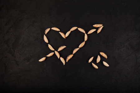 Dried Uzbek almonds or Bukhara wild almonds laid out in shape of heart with arrow on dark...