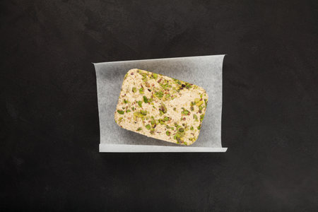 Sesame halva with pistachios on a dark background, top view. Sweet delicious plant-based dessert.