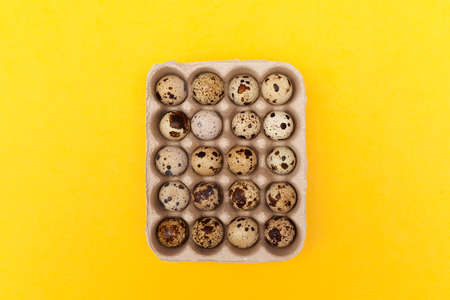 Quail eggs in package on yellow background. Top view, copy space.