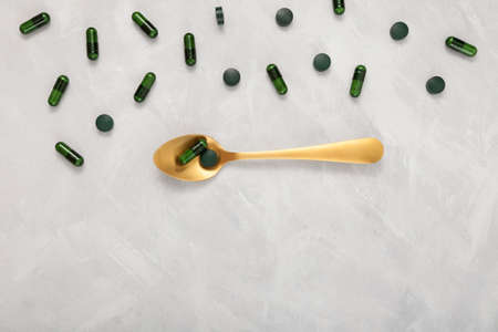 Pills chlorella and Capsules Moringa on gray background. Top view, copy space. Food supplement in golden spoon.の写真素材
