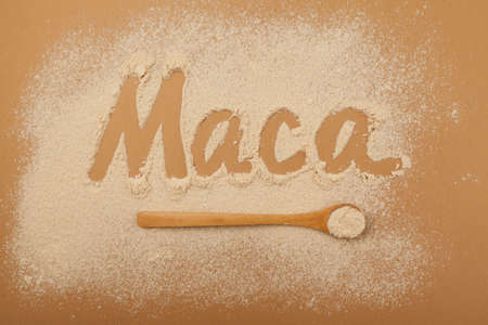 Inscription Maca of Maca gelatinized flour on beige background. Peruvian superfood, natural organic supplement. Wooden spoon with powder, top view, design element.の写真素材