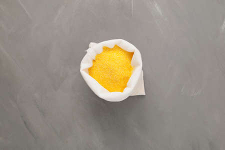 Yellow cornmeal or ground grits in white pouch on gray background. Coarse corn flour, top view, copy space.の写真素材