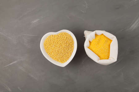 Yellow hulled millet and organic coarse flour in white bag on gray background. Top view, copy space.