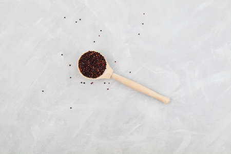 Organic black quinoa in wooden spoon on light gray background. Top view, copy space.