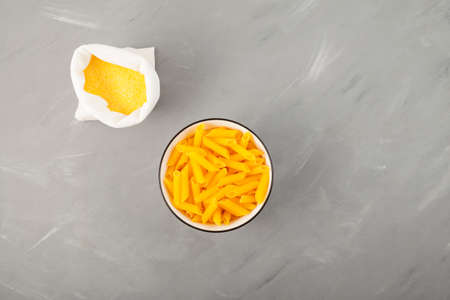 Yellow cornmeal (corn flour) and Italian pasta penne on gray textured background. Top view, copy...