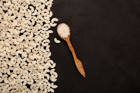 Rice flour pasta and white rice in wooden spoon, top view. Dark textured background, copy space.の写真素材