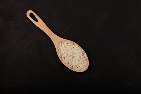 White gluten free vermicelli made from rice flour. Italian pasta in wooden spoon on dark textured background. Top view, space for text.の写真素材