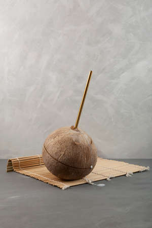 Brown coconut with drinking straw on gray background. Coconut water in real nut.