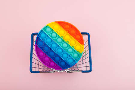 Silicone colorful anti stress toy for child in shopping basket, top view. Push Pop Bubble. Pink background, space for text. Simple dimple.の写真素材