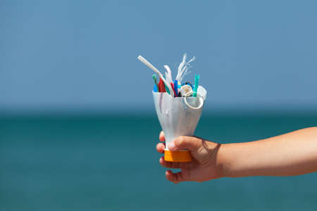 Child's hand on background of sea holds plastic garbage collected on beach. Concept - excessive...