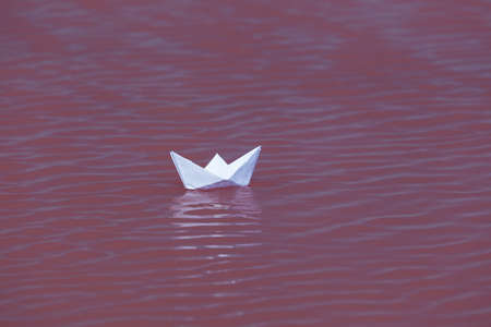 Paper boat floats on the waves on the water surface of salty pink lake. Selective focus, design element.の写真素材