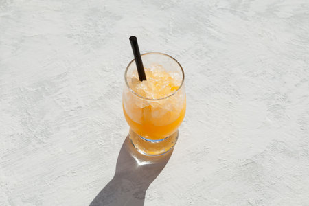 Glass of orange granizado on light table. Top view, selective focus, copy space. Crushed ice with orange juice or syrup beverage.の写真素材