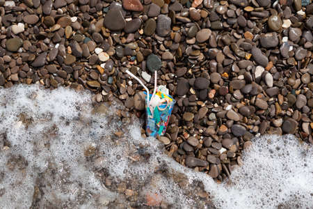 Household plastic garbage in sea. Microplastic in water. Disposable cup, fragments of packaging and cocktail drinking straws in the waves on beach.の写真素材