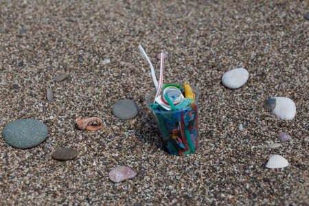 Disposable plastic cup with plastic garbage on the beach. Selective focus. Ecological catastrophe, threat to the sea and world ocean.の写真素材
