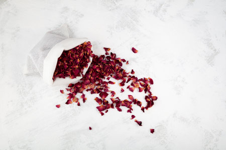 Dried rose petals in pouch, top view. Light background, copy space. Pink colored organic herb used for perfumes, cosmetics, teas and baths. Red dry petals.の写真素材
