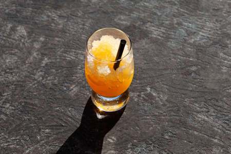 Glass of orange granizado on dark textured background. Crushed ice with orange juice or syrup...