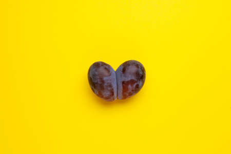 Ugly plum. Yellow background, copy space. Fused fruits, double prunes. Concept - Using for eating imperfect products. Food waste reduction.の写真素材