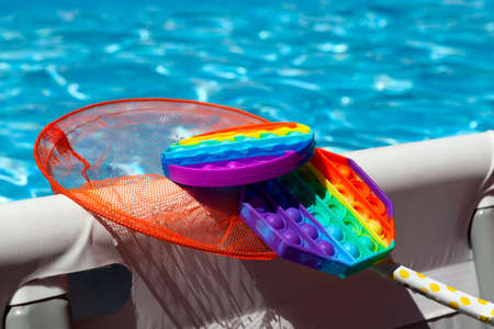 Rubber children's toy POP IT in net was caught from surface of swimming pool water.