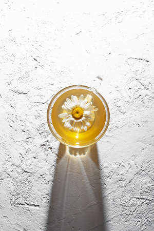 Cup of tea with chamomile flower, top view. Light textured background, shadow, copy space.の写真素材