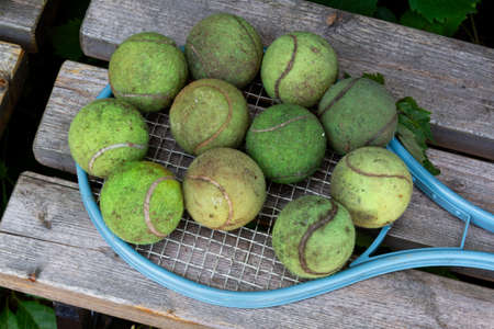 Dirty old tennis balls and vintage tennis racket on wooden bench. Close-up, top view. Leisure,...