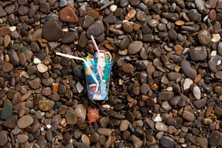 Disposable plastic garbage on wet pebbles on the seashore. Environmental problems, excessive use of disposable plastic packaging.の写真素材