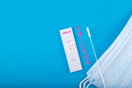Omicron, new Coronavirus variant. Fast antigen rapid test to identify coronavirus in swabs of patients. Face medical mask. Blue background, copy space.の写真素材