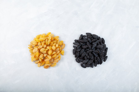 Two handfuls of raisins from dark and golden grapes on gray background, top view. Selective focus,...