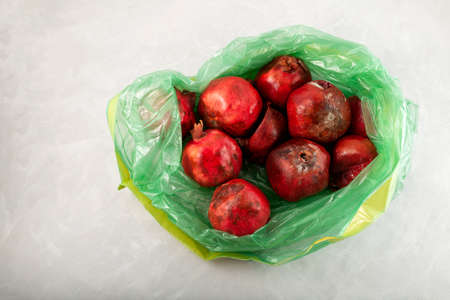 Rotten spoiled pomegranate fruits in green plastic garbage bag. Ugly moldy fruit. Improper food...