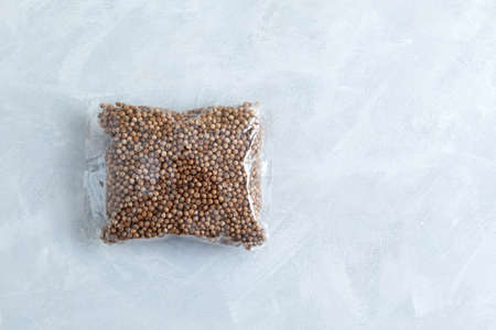 Dried coriander seeds in clear plastic bag on gray textured background. Top view, copy space.の写真素材