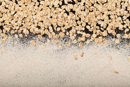 Oat flakes and Organic oat flour (ground grits) scattered on dark surface. Natural food background, design element. Top view, copy space.の写真素材