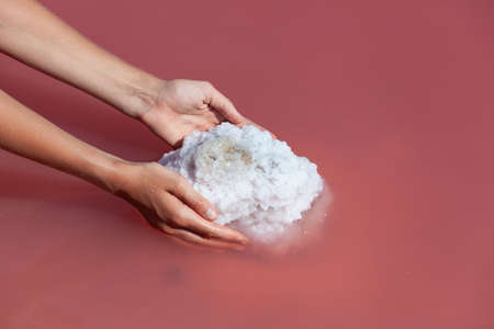 Female hands, close-up. Woman collects salt on the water surface of unique pink lake. Medicinal salt is used in cosmetology and alternative medicine. Selective focus, copy space.の写真素材