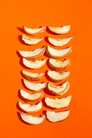 Dried apple slices or apple chips, flat lay on orange surface. Healthy vegetarian snack. Dried fruits.の写真素材