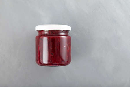 Fried or stewed beets in jar on gray textured background. Delicious ingredient for vegetarian salads...