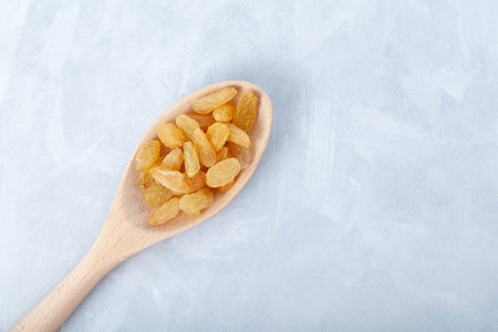 Yellow raisins in wooden spoon on gray background. Dried dehydrated grapes fruit. Selective focus, copy space.の写真素材