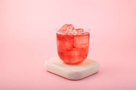 Red summer non-alcoholic drink with ice. Fruit iced tea on pink background. Rose hibiscus refreshing...