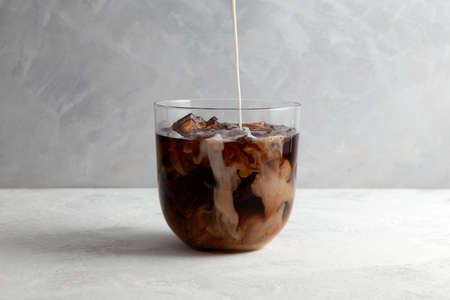 Cold iced coffee with Almond milk. Refreshing drink is poured into a clear glass. Gray background, selective focus.の写真素材