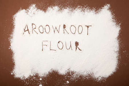 Arrowroot flour scattered on brown surface. Inscription Arrowroot flour. Top view, selective focus.